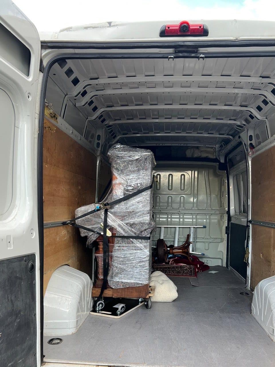Ein in Möbeldecken und Folie verpacktes Klavier steht mit Spanngurten gesichert auf einem Rollbrett im Transporter