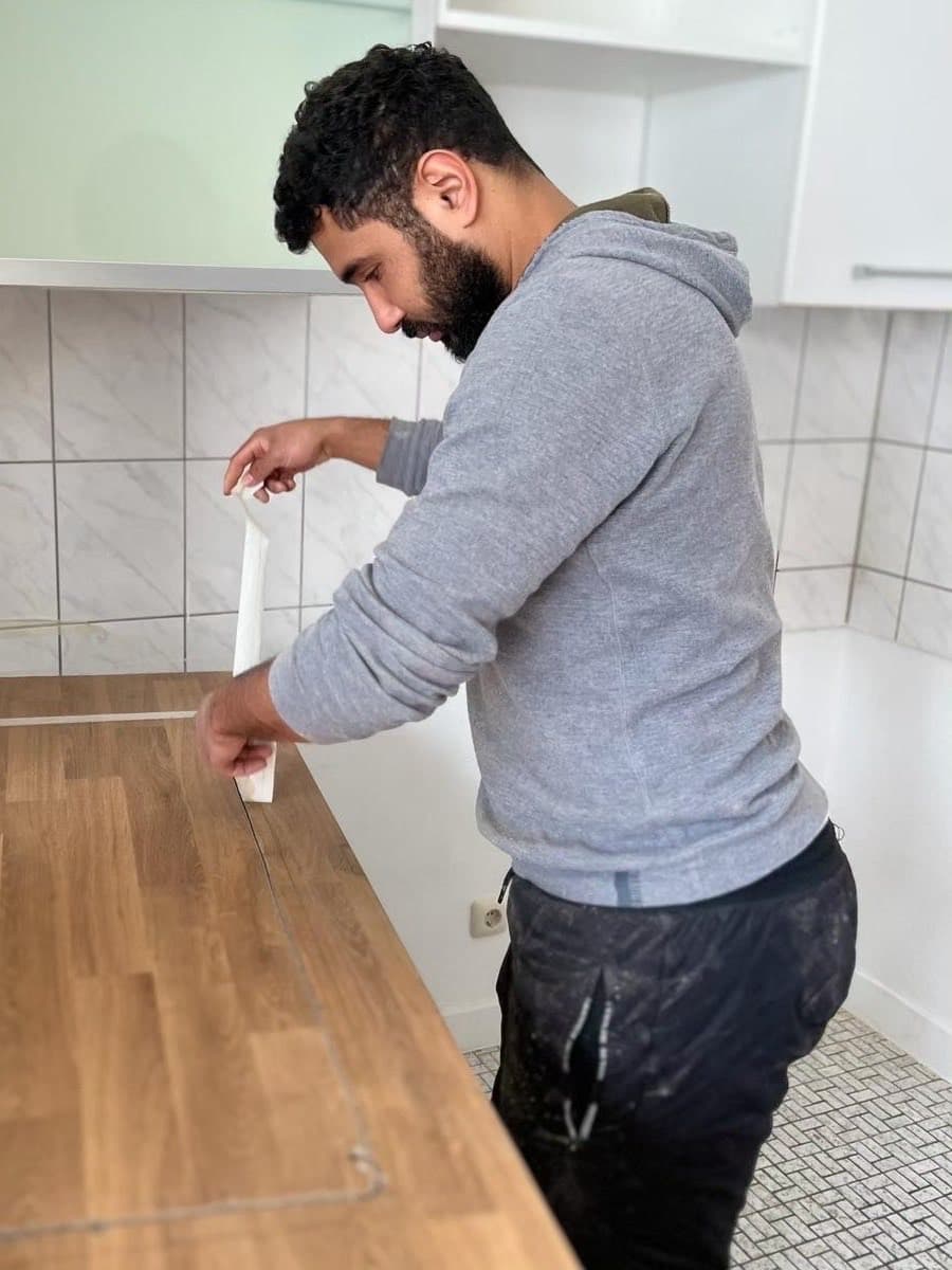 Ein Mitarbeiter zieht Dichtband an der Kante einer neuen Küchenarbeitsplatte ab