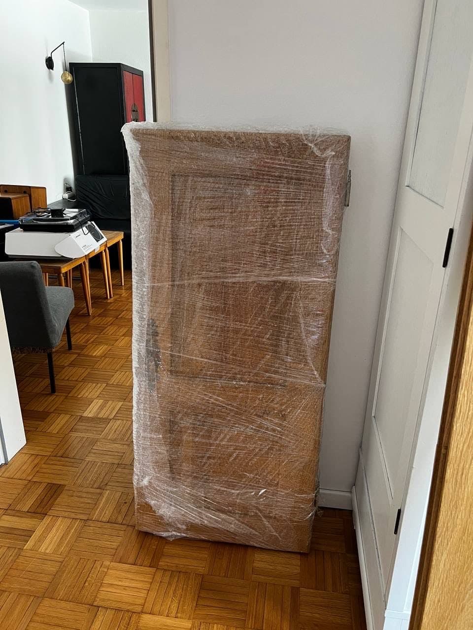 Ein hoher Holzschrank steht vollständig in Stretchfolie eingewickelt im Flur einer Wohnung