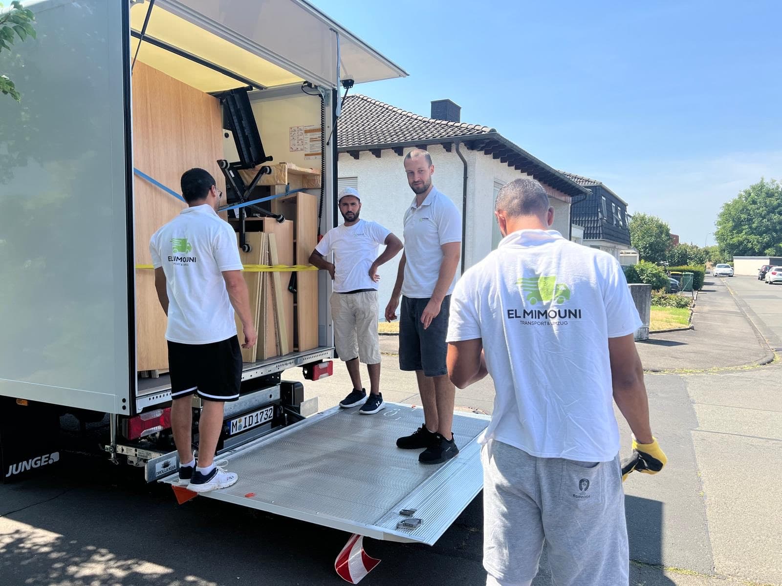 Vier Mitarbeiter in Firmen-Shirts am offenen Koffer-LKW mit ausgefahrener Ladebordwand